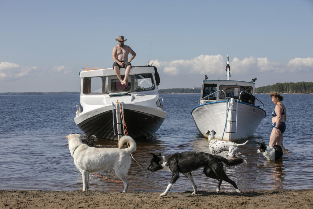 Hiekkarannan kupeessa kaksi venettä vedessä, neljä koiraa ja kaksi ihmistä.
