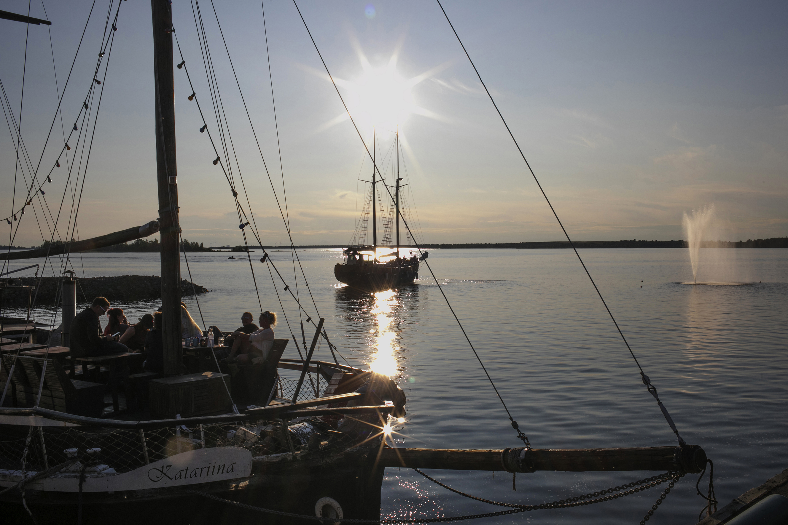 Venesatamassa purjealus rantaan kiinnitettynä ja toinen kauempana purjehtimassa.