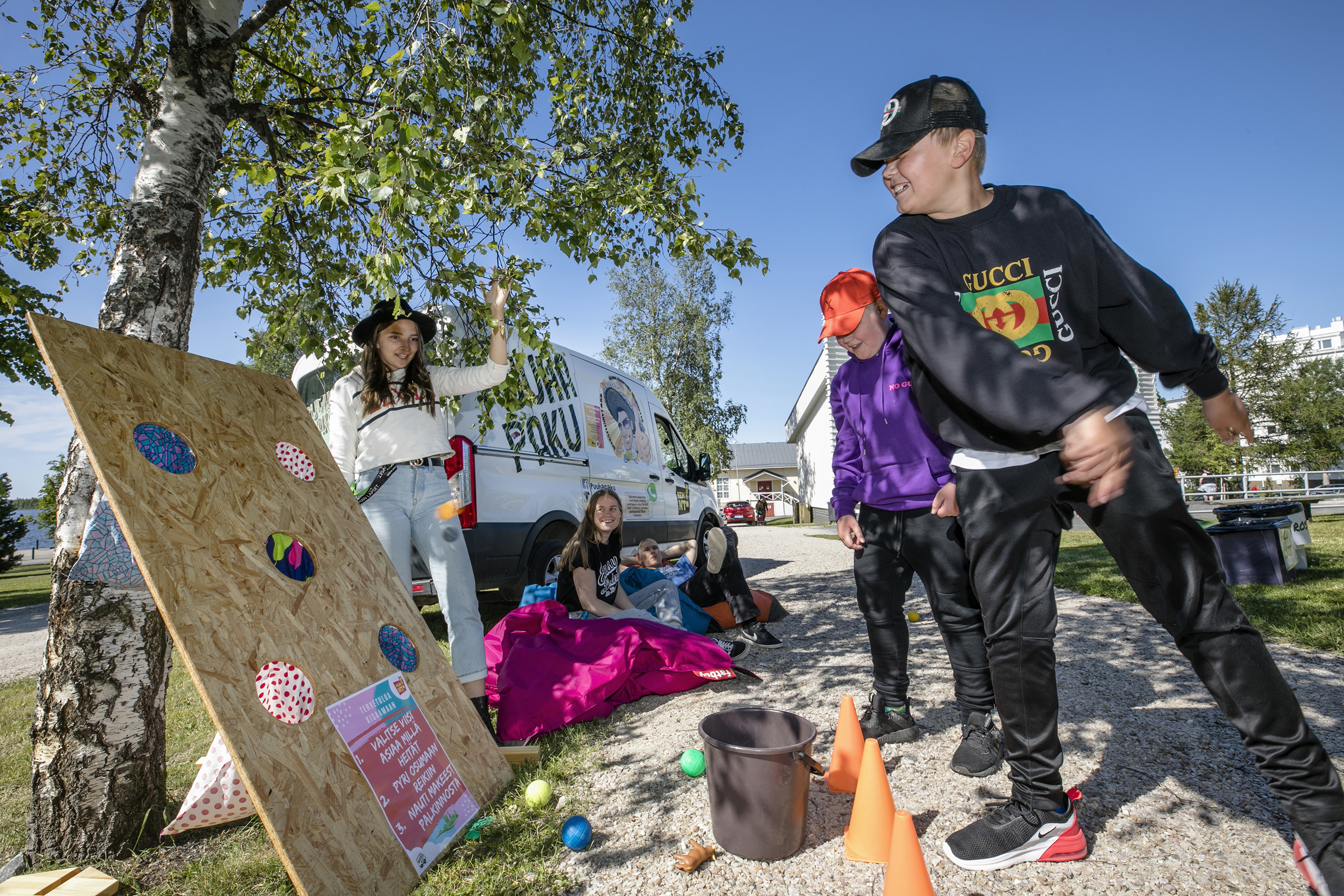 Nuorisotyön pakettiauto pysäköitynä, nuoret pelaavat ympärillä.