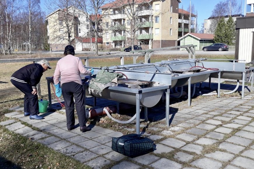 Pariskunta matonpesupaikalla, taustalla kerrostaloja.