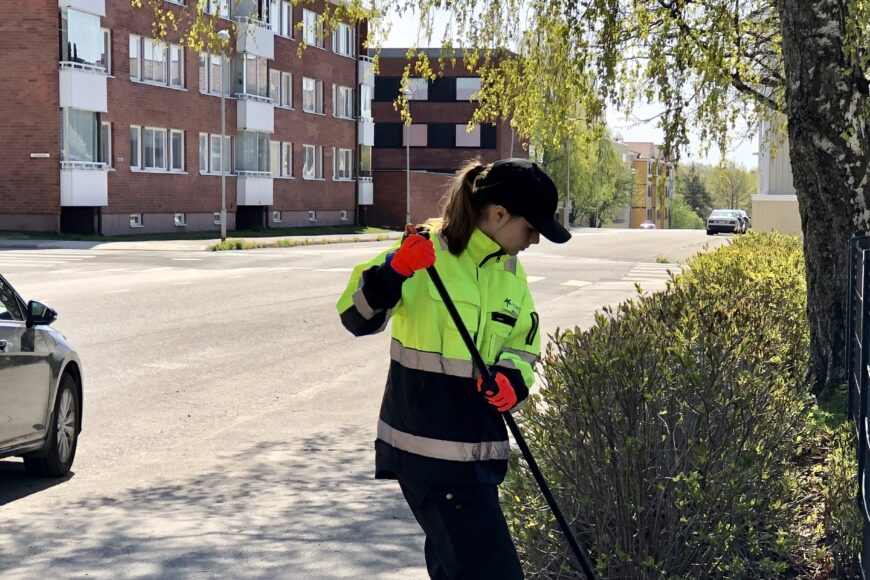 Kesätyöntekijä haravoi kadunvierustan nurmikkoa.