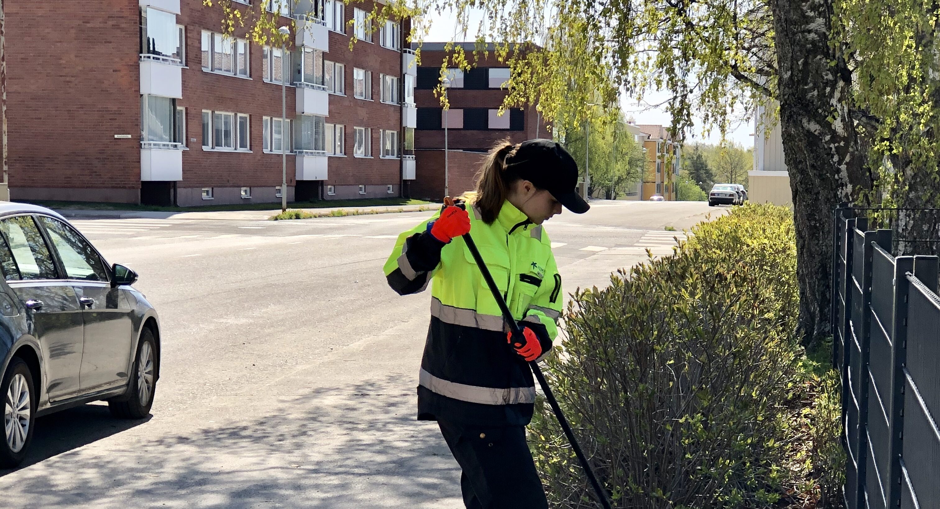 Kesätyöntekijä haravoi kadunvierustan nurmikkoa.